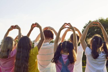 Gün batımında yaz parkında duran bir grup çocuğun kalp şeklinde jestleri. Minnettar çocuklar aşk işareti yapan arkadaşlar doğada ellerini kaldırıyorlar. Çocuk koruma kavramı
