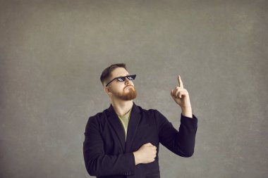 Komik adam çok zekice bir fikir düşünmüş. Takım elbiseli genç adam ve haydut hayatı 8 bit gözlüklü parmağını gri arka planda izole bir şekilde gösteriyor.