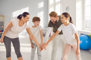 Mutlu ebeveynler ve çocuklar aile spor yaparken eğleniyorlar. Gülümseyen anne, baba ve çocuklar spor salonunda el ele tutuşuyorlar. Spor, destek, motivasyon kavramı