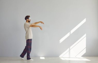 Gri duvar arkasında, uyurgezer, uyurgezer ve maske takan genç bir adamın tam boy portresi. Uyurgezerlik, uykusuzluk ve uyku sorunları kavramı.