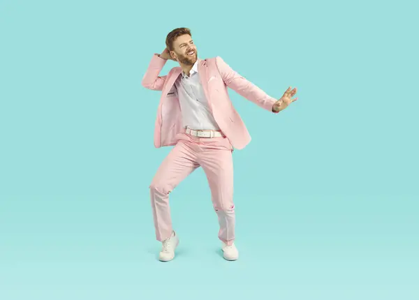 Young guy relaxing and having fun. Full length shot of a happy, cheerful, funny young man wearing a trendy pink party suit dancing isolated on a bright blue colour background