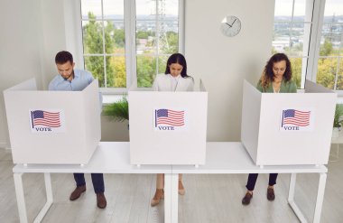 Kendine güvenen bir grup genç Amerikan vatandaşı oy verme merkezinde sırada bekliyor ve oy verme kabininde ABD bayrakları var. Seçim günü oy kullanma merkezindeki insanlar. Demokrasi kavramı.