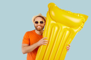 Mavi arka planda, plaj kıyafetli mutlu bir adam tatilden ya da yaz güneşinde elinde bir plaj yatağı olan hafta sonu kaçamağından hoşlanıyor. Tatillerin ve seyahat maceralarının neşesi ve rahatlığı.