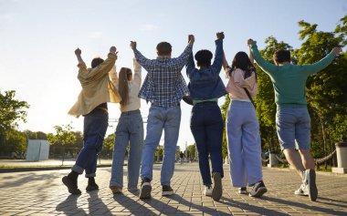 Mutlu arkadaşlar gün batımında kollarını kaldırarak bir arada duruyorlar. Bir grup erkek ve kadın arkadaş parkta yürürken el ele tutuşup arkadan bakıyorlar. Arkadaşlık, takım çalışması, başarı konsepti