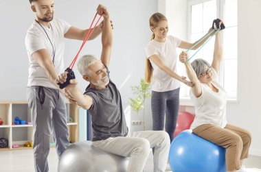 Doktor ve antrenör, rehabilitasyon sırasında fizik tedavi egzersizleri yapan yaşlı ve yaşlı bir çift hastaya rehberlik ediyor. Yaşlılar için egzersiz programları, refahın ve yaşam kalitesinin arttırılması.