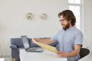 İş adamı bir mektup alır. Ciddi sakallı bir adam çalışma masasında oturuyor evinde dizüstü bilgisayarla ve içinde iş mektupları olan bir zarfı açıyor.