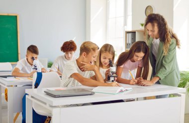 Genç bayan öğretmen bir ders sırasında bir grup öğrenciye yardım eder. Atmosfer takım çalışması, okul başarısı ve eğitim işbirliğine ortak adanmışlık ile suçlanıyor..