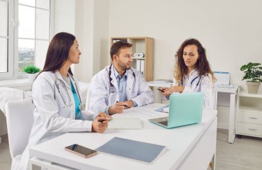 Doktorlar, klinikteki çalışma masasında dizüstü bilgisayarla oturup tanı koyma, test sonuçlarını kontrol etme ya da tedavi planlama konularını tartıştılar. Sağlık personeli, sağlık ve takım çalışması kavramı.