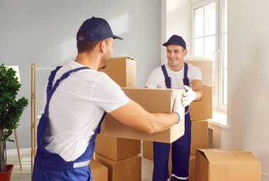 Taşıma şirketindeki mutlu işçiler yeni daireye eşyalarını koydular. Teslimat şirketinden iki gülümseyen adam müşterilerinin taşındığı evin içine karton kutular koydu.