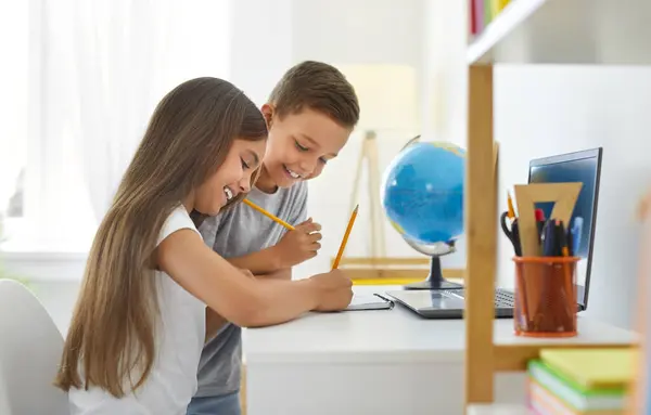 快乐的孩子们坐在桌旁 用铅笔画画 小弟弟和小妹妹在笔记本上写字时的侧视图肖像 创造性活动 家庭教育概念 图库照片
