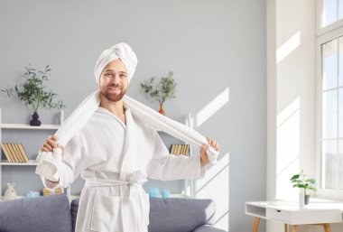 Havluyla bornoz giymiş mutlu ve gülümseyen bir adamın evdeki banyo ve duştan sonraki sabah rutinini anlatan bir portresi. Neşeli ve mutlu görünüyor. Önümüzdeki güne hazır..