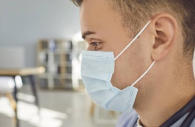 Medikal ofiste duran düşünceli doktor ya da mavi maskeli hemşire portresinin yan görüntüsü. Klinikte fotokopi alanı olan genç bir erkek doktor. Sağlık ve Tıp Konsepti.