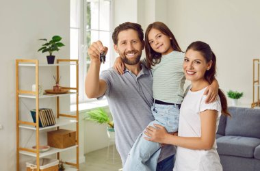 Mutlu ebeveynler, baba, anne ve kız çocukları ellerinde ev anahtarları ve yeni dairede kameraya karşı neşeli görünüyorlar. Aile daire almaktan zevk alıyor. Emlak ve taşınma günü konsepti.