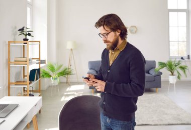 Ciddi bir adam akıllı telefonu mobil uygulamaları taramak, çalışmak, haber okumak, sohbet etmek, internetten alışveriş yapmak veya internette bilgi aramak için kullanır. Adam ofisteki ya da evdeki cep telefonuna bakıyor..