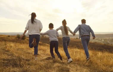 Büyük neşeli aile gün batımında sarı tarlada oynuyor. Günbatımında gökyüzü güzel doğa sarı tarla ebeveynleri ve çocuklar açık havanın güzelliğini sever mutlu doğa günbatımında aile