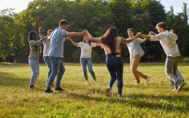 Bir grup mutlu arkadaş yazın tadını çıkarıyor ve güneşli parkta eğleniyorlar. Sekiz neşeli, çok kültürlü insan el ele tutuşup yeşil çimlerin üzerinde dans ediyor.