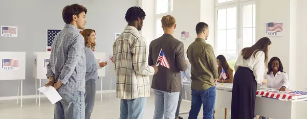 大批各种各样的人在选举日当天在投票站登记 手里拿着美国国旗 美国选民排队站在美国公民的投票中心 图库图片