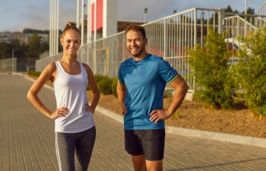 Spor giyim kuşamaları giyen mutlu, genç bir çift spor egzersizlerinden sonra şehir parkında dinleniyor. Doğa sporu, açık hava sporu ve sağlıklı yaşam tarzı konsepti.