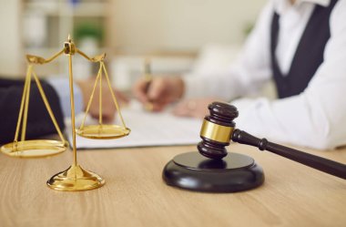 Adaletin altın pullarını kapatın ve avukatlık bürosundaki bej çalışma masasının üzerinde koyu kahverengi tahta tokmak, arka plandaki müşteriye danışmanlık yapan hukuk uzmanı. Hukuki danışmanlık, hukuki hizmet kavramı
