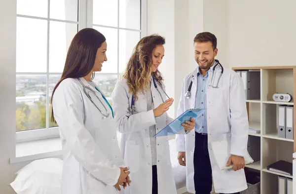 由3名身穿白衣的年轻医生组成的快乐团队站在医院或诊所与病人讨论诊断或治疗计划 医务人员和保健概念 图库图片