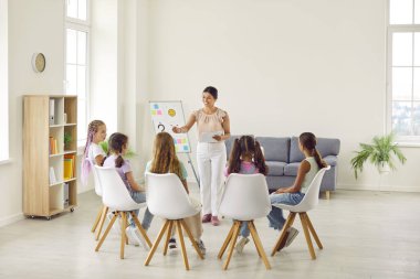 Bir grup ilkokul çocuğu için psikolojik eğitim veren arkadaş canlısı genç bir kadın sınıfta bir çemberde oturuyor ve psikolog hoparlörlerini dinliyor..