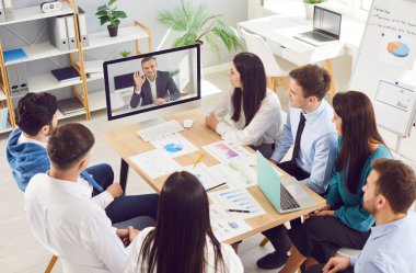 İş adamlarından oluşan bir grup, online video konferans odasında modern ofisteki çalışma masasında bilgisayardan online video görüşmesi yapıyorlar. İş teknolojileri kavramı.