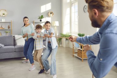 Neşeli gülümseyen çocuklar, aileleriyle birlikte evdeki salonda halatla oynuyorlar. İçeride çocuklarla eğlenen neşeli, genç bir aile. Mutlu aile ve eğlence konsepti.