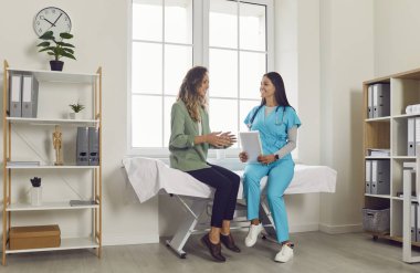 Mutlu kadın doktor hastayla hastanedeki sağlık hizmetleri hakkında konuşuyor. Etkileşimleri sıcaklıkla ve anlayışla dolu, hasta tıbbi bakımının özünü sembolize ediyor..