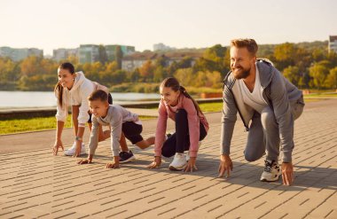 Mutlu bir aile şehir caddesinde spor yapıyor. Gülümseyen anne, baba ve çocuklar koşmaya hazırlanıyor. Sportif anne, baba ve çocuklar yarış için sıraya girdiler.