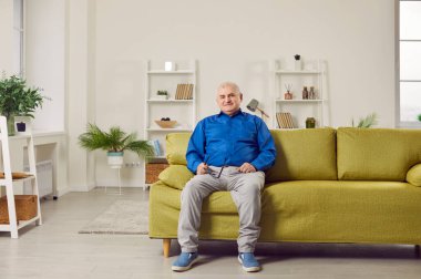 Evdeki kanepede oturan iyimser yaşlı adam. Neşeli gri saçlı son sınıf öğrencisi oturma odasındaki modern rahat koltukta gözlük takıyor. Yaşlılar ev hayatı konsepti