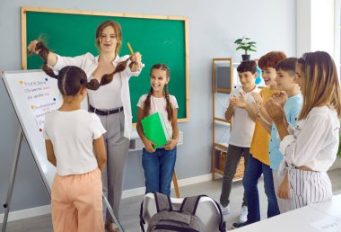 Mutlu çocuklar ve öğretmenler sınıfta eğleniyorlar. Eğitmen ve öğrenciler sınıf kurulunun önünde oyun oynuyorlar. Öğretmen kız öğrenciyi örgülerinden tutuyor ve sınıf arkadaşları kızı alkışlıyor.