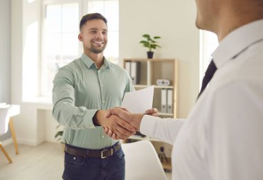 Two happy young men shaking hands and smiling. Two people meet in the office, establish partnership relations, make a lucrative business deal and exchange handshakes. Cooperation, teamwork concept