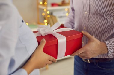 Giving present hand closeup, people in love holding red surprise gift box with ribbon, sharing special romantic moment. Valentine day existing emotion, couple special for birthday, holiday, new year 