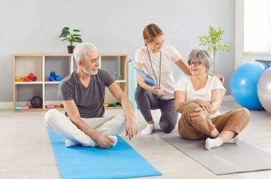 Active happy elderly people and young coach, senior spouses sitting in yoga studio floor in lotus position, practice meditation exercise to relieve stress or renew energy, following healthy lifestyle