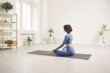 Yogi sportif çekici kadın yoga yapıyor Ardha Padmasana egzersizi yapıyor, Mudra hareketleriyle Yarım Lotus pozu veriyor spor kıyafetleriyle spor kıyafetlerini giyip beyaz yoga stüdyosunda, evinde mindere oturuyor.