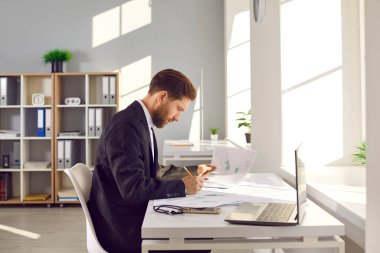 Ofiste çalışan meşgul bir erkek mimar. Şehir kadastro haritalarıyla birlikte masada oturan genç adam, bölge hakkında bilgi alıyor, yeni inşaat alanları ve inşaat planının geliştirilmesi konusunu düşünüyor.