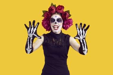 Şeker kafa makyajlı güzel bir kız Boo diyor. Yüzü boyalı, çiçeklerden yapılmış çelenkler giyen, avuçlarını iskelet eldivenlerle gösteren siyah elbiseli genç bir kadın. Ölüm Günü, Cadılar Bayramı konsepti