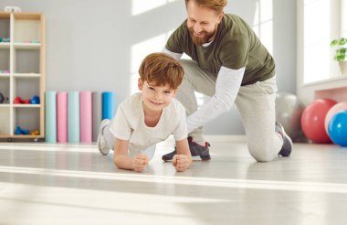 Çocuk kalas pozisyonunu korumaya odaklanıyor. Babası küçük oğlunu parlak spor salonunda eğitiyor ve ona tahta pozisyonunda durmayı öğretiyor. Çocuklara sağlıklı yaşam tarzını küçüklükten itibaren öğretme kavramı.