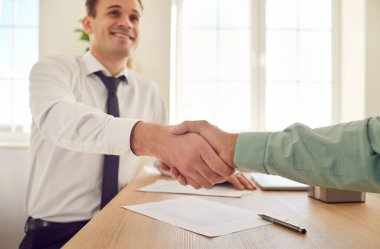 Mutlu iş adamı ofisteki bir müşterisine ya da meslektaşına el sıkışır. Bu jest, başarılı bir anlaşmanın, ortaklığın, anlaşmanın veya takım çalışmasının tamamlanmasını sembolize eder..