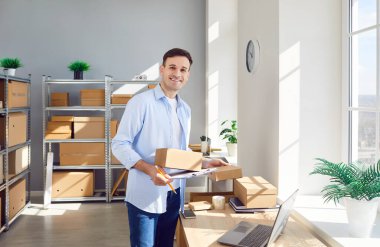 Depoda çalışan küçük bir işletme sahibi stokları ve envanterleri kontrol ediyor iş yerinde duruyor ve depodaki müşteriler için kamera hazırlama sırasına bakıyor. Teslimat ve depo işi konsepti.