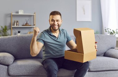Mutlu adam kanepede oturuyor ve evde bir karton kutu açıyor, bir paket, paket ya da hediye alıyor. Onun ifadesi bir teslimat veya alışveriş sürprizinden gelen mutluluk ve heyecanı gösteriyor..