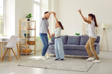 Neşeli insanlar evde eğleniyor. Canlı müzikle dans eden mutlu ve hayat dolu bir aile. Genç enerjik anne, baba ve çocuk modern ferah ve rahat oturma odasında dans ediyor.