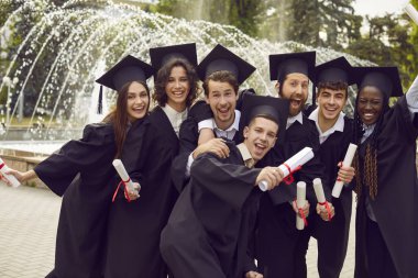 Tebrikler, mezun. Mutlu, neşeli, çok ırklı, çok ırklı, öğrenci şapkalı ve cüppeli arkadaşlar üniversite mezuniyetinin olumlu anılarını hatırlamak için fotoğraf çekiyorlar.