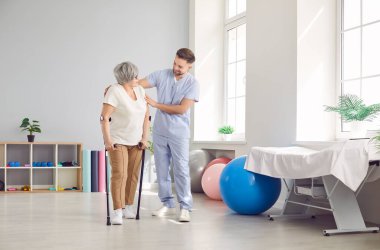 Genç erkek bakıcı, engelli kadın hastaya yürümesi için yardım eden hemşire destekleyici egzersiz terapisi öğreten fizyoterapi hemşiresi, rehabilitasyon tedavisi.