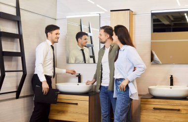 Genç ve mutlu bir çift evlerinde banyo için lavabo ve tesisat seçiyor ve banyo mağazasında erkek arkadaş canlısı bir satıcıyla duruyor. Erkek ve kadın inşaat piyasasında erkek satıcıya danışıyor..