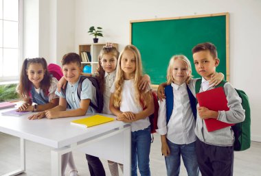 Okulun ilk gününde mutlu çocuklar. Günümüz beyaz sınıfında yeşil karatahtayla dikilen bir grup sıradan kıyafetli ilkokul öğrencisi. Okula, öğrenmeye ve eğitim kavramlarına geri dönmek.
