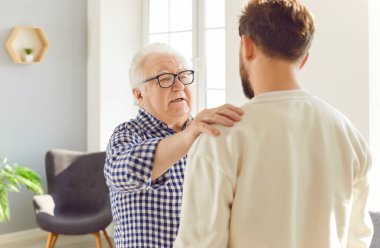 Yaşlı baba ve yetişkin oğul bir arada duruyorlar babalar elleri oğullarının omuzlarında birbirlerine mutlu bir baba gibi bakıyorlar. Babalık anı, aile bağlarının sıcaklığını yansıtır.