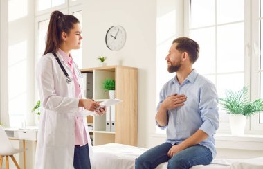 Genç adam doktor muayenehanesinde kanepede oturuyor ve klinikteki muayene sırasında göğsünü doktora gösteriyor. Hastaları dinleyen doktorlar şikayetçi..