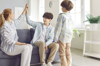 Mutlu gülümseyen anne, evdeki oturma odasında oturan genç çocuğuna beşlik çakıyor. Genç ebeveynler çocuklarla yapılan başarılı anlaşmayı kutluyorlar. Aile eğlencesi ve takım konsepti.