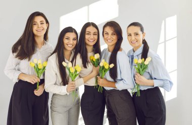 Uluslararası kadın gününü kutlayan ellerinde çiçeklerle güzel mutlu kadınların portresi. Sarı lale buketleri tutan beş zarif kadın parlak odada yan yana durur ve kameraya gülümserler..